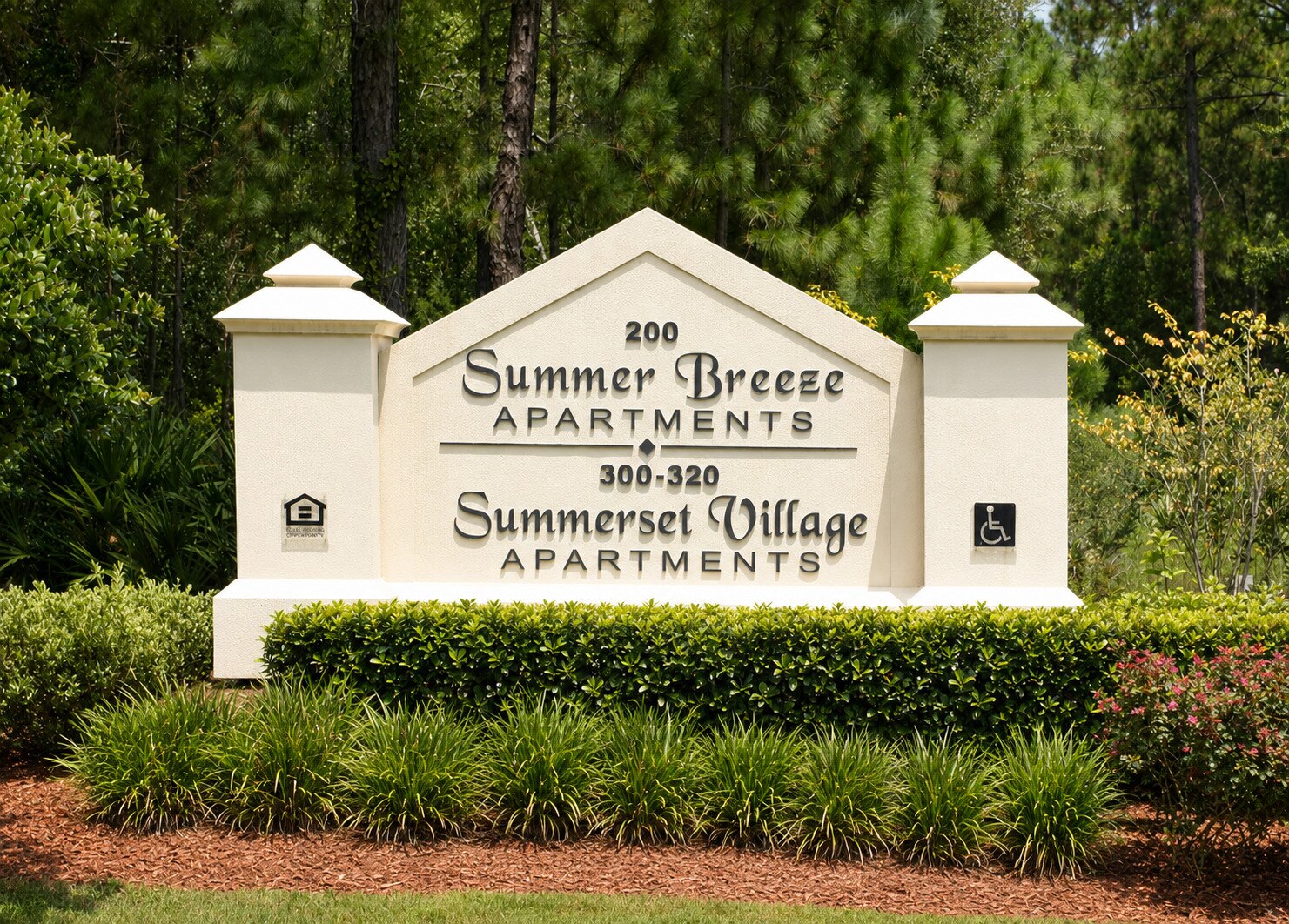 Maintained apartment community monument framed by trimmed shrubs, ornamental grasses, and fresh mulch